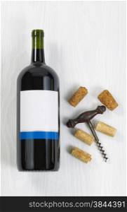 Vertical image a large bottle of red wine with an antique corkscrew with old corks on white wood.