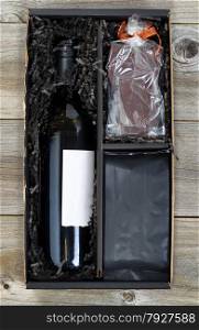Vertical image of a gift box with wine, chocolate and bag of coffee on top of rustic wood.