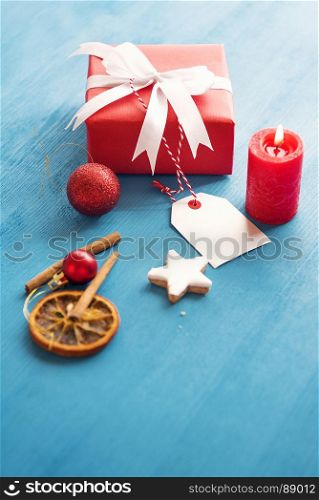 Vertical image of an elegant gift wrapped with red paper and tied with white ribbon and bow, with an etiquette attached to it, in a Christmassy decor.