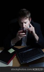 Vertical image of business man, drinking alcohol, working late with black background