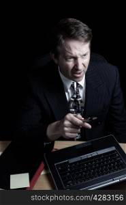 Vertical image of business man, expressing anger while looking at computer screen, working late with black background