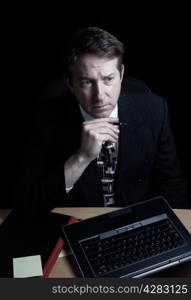 Vertical image of business man, looking at computer screen while holding pen, working late with black background