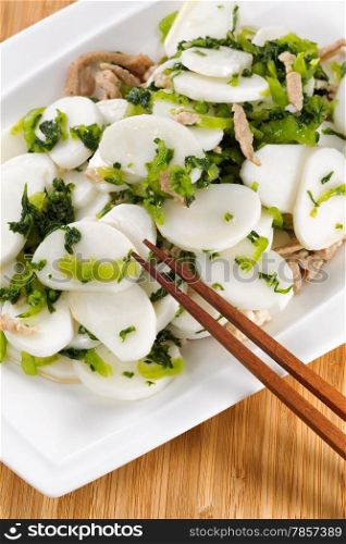 Vertical image of Chinese rice noodles with pork slices in white plate with natural bamboo background