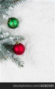 Vertical image of Christmas ornaments, red and green, hanging from a real Blue Spruce tree branch placed on snow