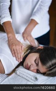 Vertical image of female Reiki therapist holding hands over shoulders of the patient and transfer energy. Peaceful teenage girl lying with her eyes closed. Alternative therapy concept of stress reduction and relaxation.  