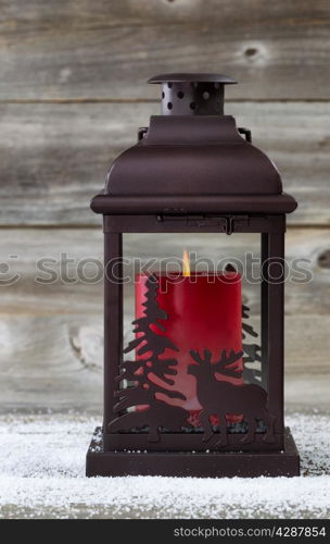 Vertical image of holiday lantern with burning red candle inside on rustic wood