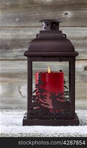 Vertical image of holiday lantern with burning red candle inside on rustic wood
