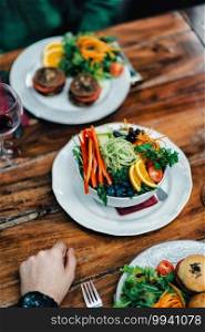 Vertical image of vegeterian dinner served on wooden table in restoran. Delicious vegetarian burger and  mixed organic salad on white plate. 