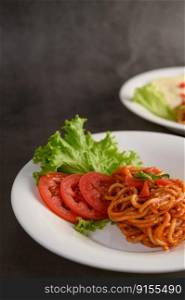 Vertical image, Selective focus the Stir fried spaghetti with tomato sauce and tomato slice with lettuce in white plate, copy space