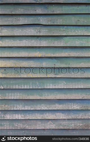 vertical part of shed wall consisting of old horizontal wooden planks with faded green paint and yellow moss