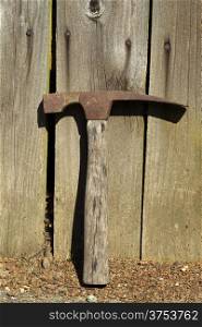 Vertical photo of an old hammer lying against aged fence
