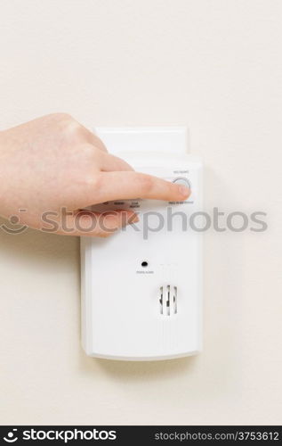 Vertical photo of carbon monoxide alarm with female hand testing the system