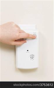 Vertical photo of carbon monoxide alarm with female hand testing the system