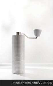 Vertical photo of light gray manual coffee grinder on white table.