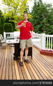 Vertical photo of mature man holding glass of beer with barbecue cooker and seasonal trees in background
