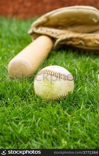 Vertical photo of old baseball, bat and glove with grass and red baseline in background
