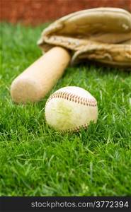 Vertical photo of old baseball, bat and glove with grass and red baseline in background