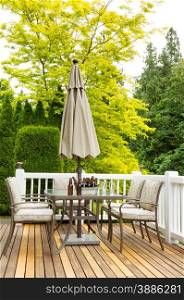 Vertical photo of outdoor patio table with cold bottled beer in bucket and drinking glasses on cedar wood patio. Colorful trees in background.