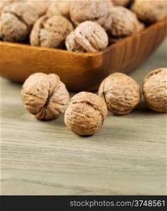 Vertical photo of whole walnuts lying on faded wood with additional nuts and wooden bowl in background