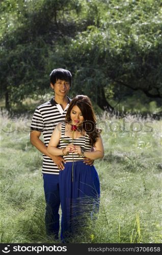 Vertical photo of young adult couple with woman looking at single red rose in the middle of a bright green grass field