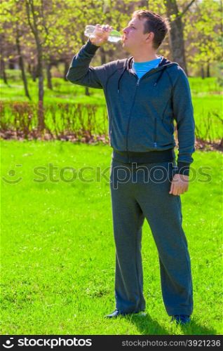 Vertical portrait of a man drinking water on a green lawn