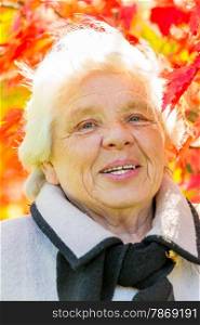 Vertical portrait of an elderly woman on a background of red leaves