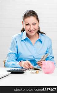 Vertical portrait of businesswoman with money and piggy bank sitting at table