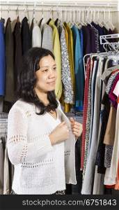 Vertical portrait of mature Asian woman in walk-in closet putting on her white sweater