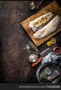 Vertical seafood background with raw cod fillet with lemon slices and herbs on rustic background with cutting board and knife, top view. Fish cooking preparation. Healthy diet food. Copy space