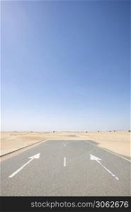 Vertical shot of an empty road covered by sand in the desert with large copy space in the blue sky. Road in the desert