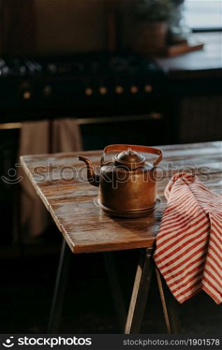 Vertical shot of steel kettle on wooden table in cozy room. Old ancient aluminium teapot to make tea. Vintage houseware.