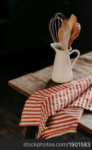 Vertical shot of vintage kitchen utensils in white ceramic jar on wooden table. Home kitchen decor. Kitchenware for cooking. Household items