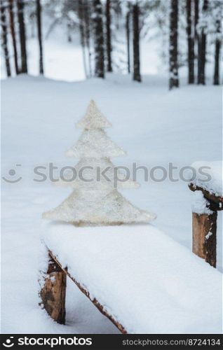 Vertical shot of white artificial fir tree on bench covered with snow, in winter frosty forest. Holidays decoration. Season concept. Holiday. Wonderful winter