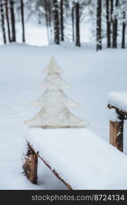 Vertical shot of white artificial fir tree on bench covered with snow, in winter frosty forest. Holidays decoration. Season concept. Holiday. Wonderful winter