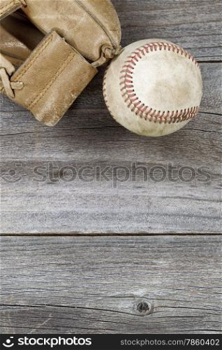 Vertical top view angle of old baseball and weathered leather mitt on rustic wood. Plenty of copy space.