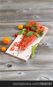 Vertical view of raw red salmon, skin side down, on maple wood grilling plank with seasoning and other herbs