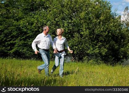 Very active mature or senior couple running over the grass on a meadow in summer