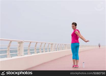 very active young beautiful woman stretching and warming up on the promenade along the ocean side to keep up her fitness levels as much as possible