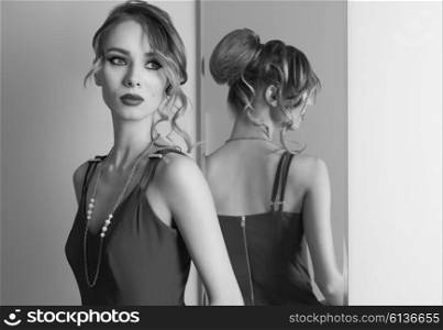 very beautiful female with hair-style and make-up trying red dress in changing room near mirror. Fashion portrait in black and white