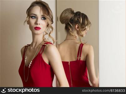 very beautiful female with hair-style and make-up trying red dress in changing room near mirror. Fashion portrait