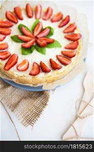 Very beautiful summer cheesecake decorated with strawberries - stands on a white wooden table.. Very beautiful summer cheesecake decorated with strawberries - stands on a white wooden table