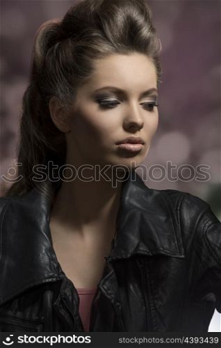 very beautiful young brunette female posing in dark fashion shoot with creative hair-style and modern leather jacket
