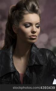 very beautiful young brunette female posing in dark fashion shoot with creative hair-style and modern leather jacket