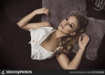 very cute and sweet blond young woman , laying on the sofa , she has elegant dress , and long hair . she is looking up with a dreaming expression