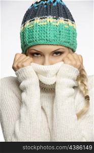Very cute woman with tress and winter dress covering her face with sweater and looking in camera with smiling eyes