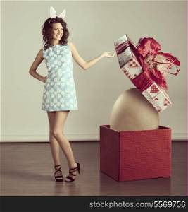 very cute young woman in spring ligh blue dress, with easter bunny ears ,near a big box with egg inside