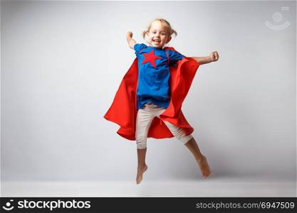 Very excited little girl dressed like superhero jumping alongside the white wall.. Very excited little girl dressed like superhero jumping alongside the white wall