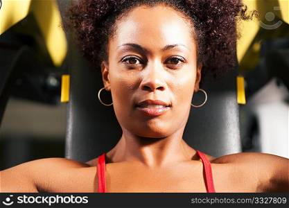 Very fit and beautiful African-American woman in a gym working out and lifting weights on an exercising machine