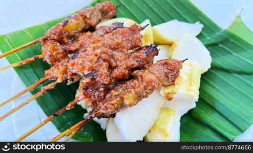 very flavorful beef satay meat grilled over charcoal served with peanut sauce and rice cake on banana leaf