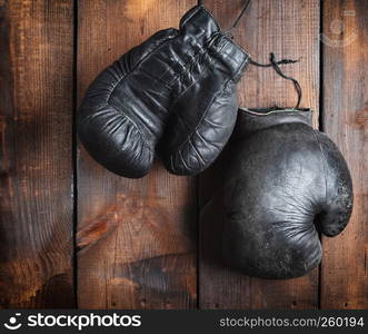 very old black boxing gloves on a brown wooden background, top view